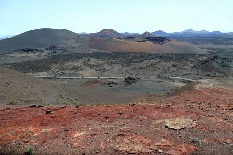 Svart lavafält med kraterkullar och rödbrun jord på Lanzarote