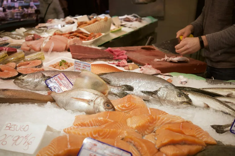 Fiskdisk med färsk fisk på is och en försäljare som styckar