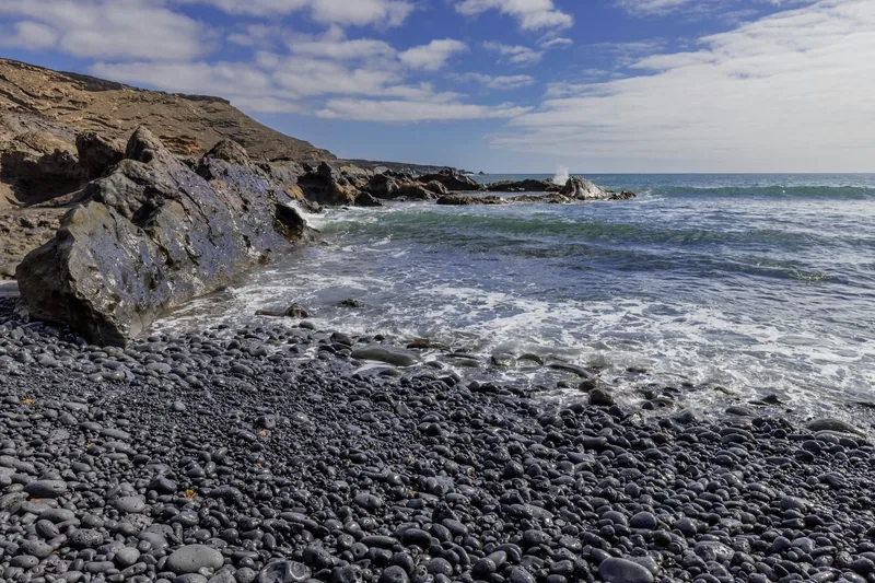 Vågor som slår in mot en strandkant av svarta lavastenar på Lanzarote
