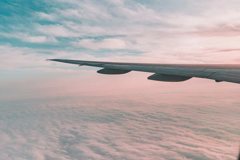 Vinge på ett flygplan mot rosa himmel högt över molnen